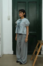 Woman wearing a checkered top and striped pants standing in front of a dark green door.