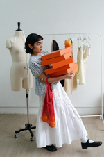Person holding orange boxes in a room with a mannequin and clothing rack.