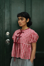 Woman wearing a red and white checkered blouse against a dark green door.