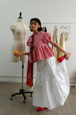 Person in a checkered top and white skirt standing next to a mannequin and clothing rack.