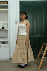 Woman wearing a white top and beige skirt standing in a room with a green door and wooden step stool.