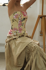 Person wearing a floral dress with a beige skirt sitting on a chair.